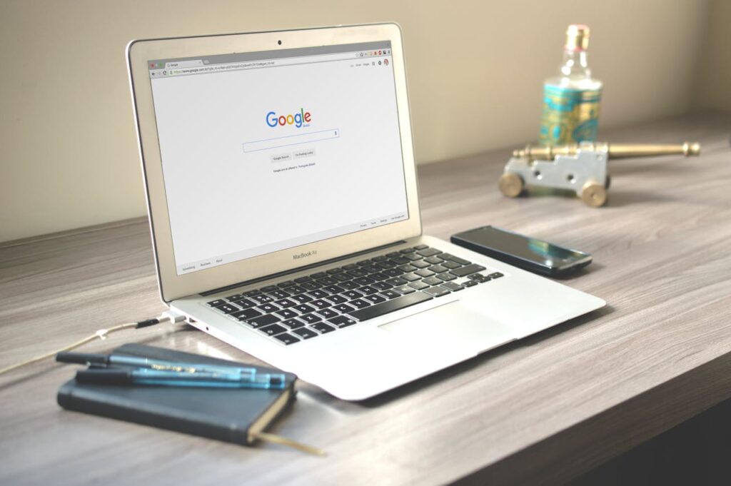 pexels-photo-67112 A neat workspace featuring a laptop displaying Google search, a smartphone, and a notebook on a wooden desk.